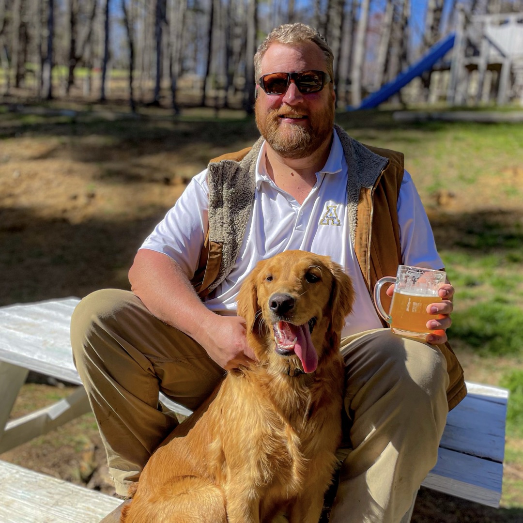 Andrew Plyler with his golden retriever, wearing an Appalachian State polo